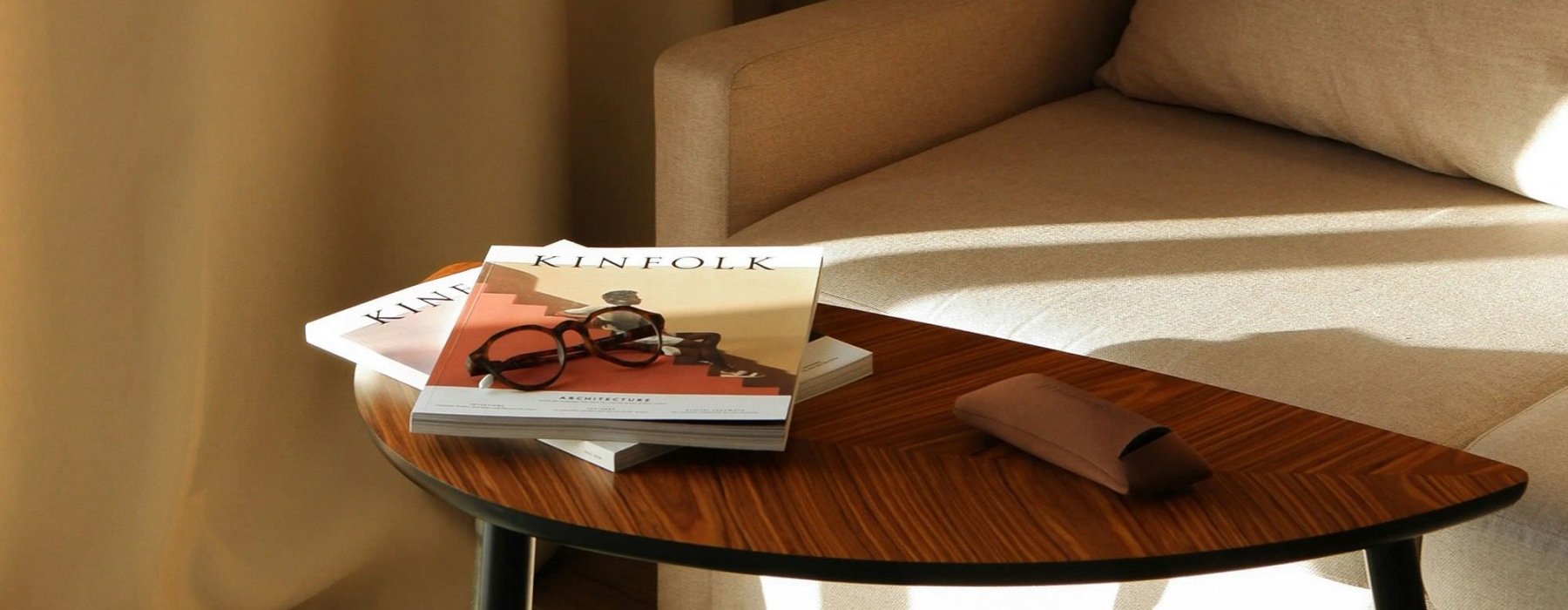 A table with a book and glasses on it next to a couch in the sunlight.